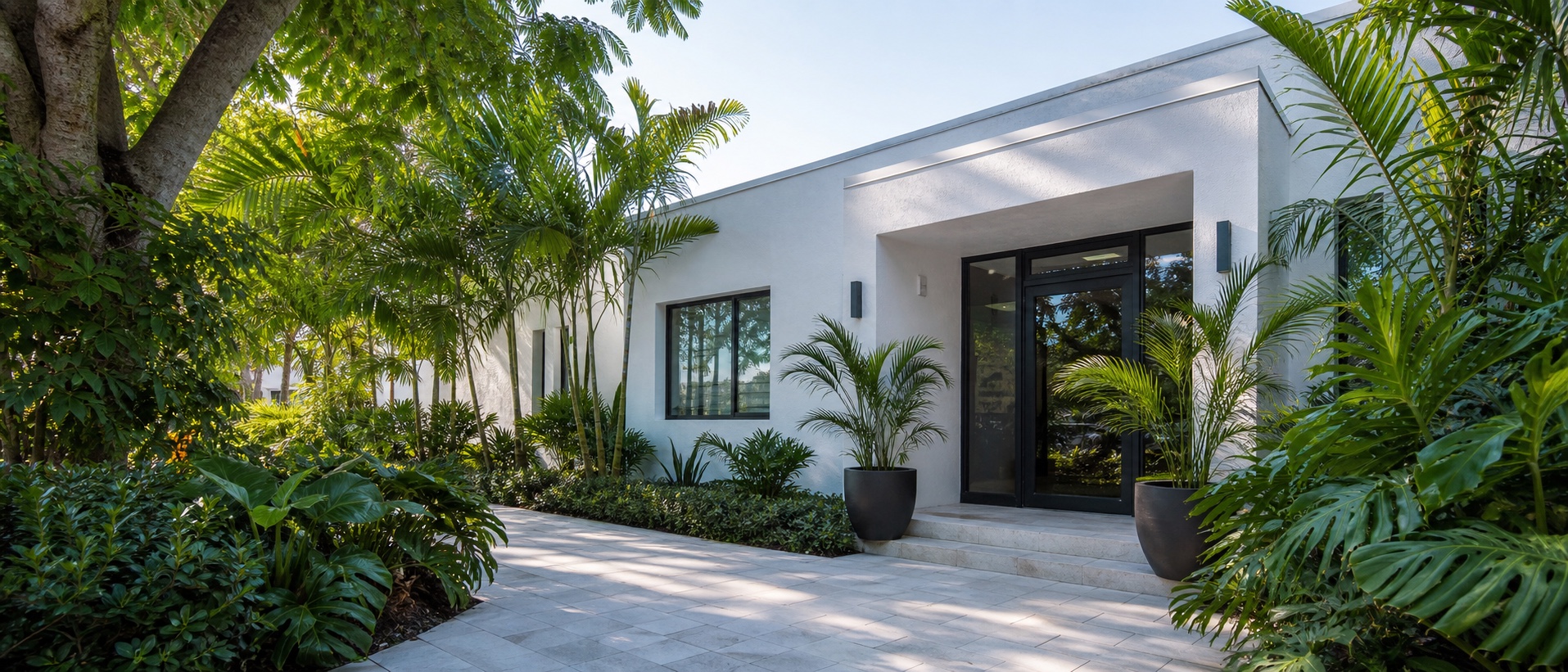 Tropical planting frames the pale-stone walkway and glass entry of a small Fort Lauderdale design studio